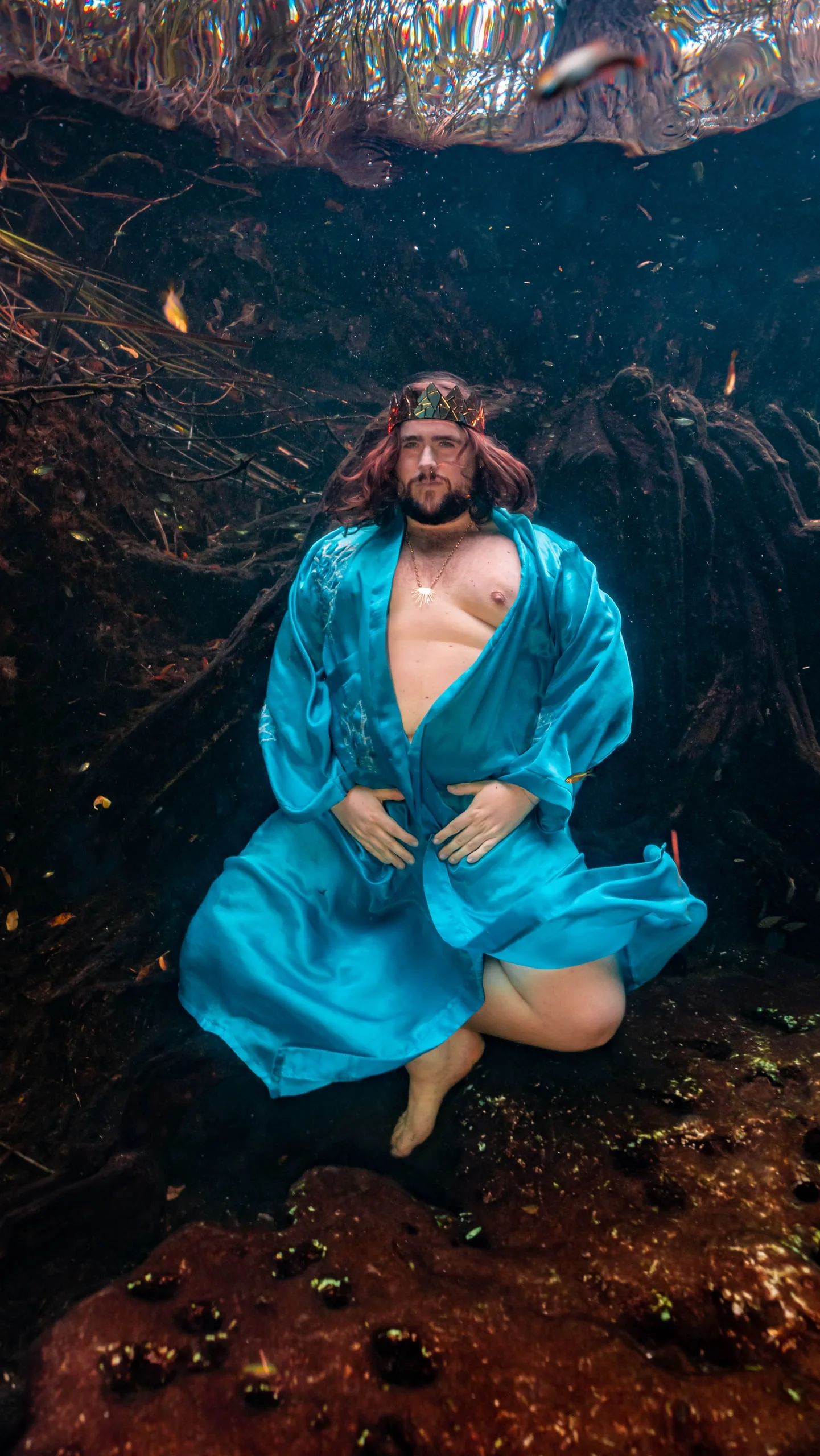 A figure in a turquoise robe suspended among cenote roots