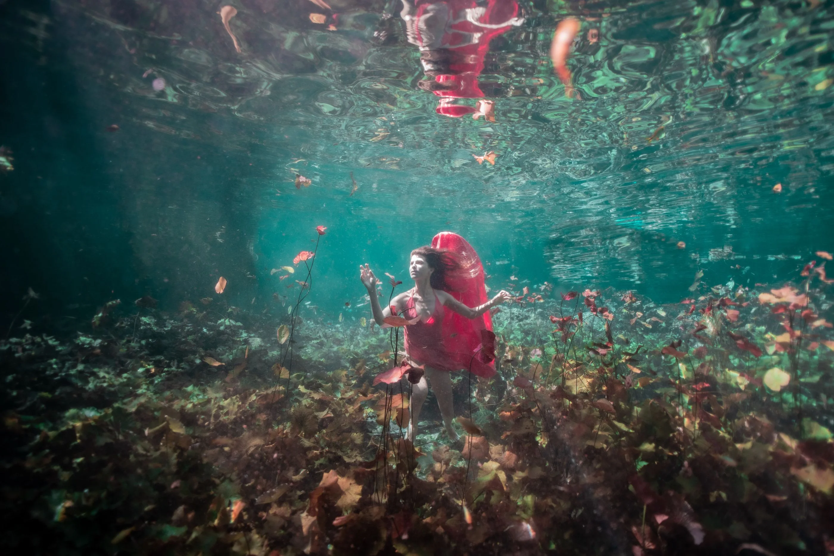 Woman in a red dress standing among leaves on the floor of a Tulum cenote