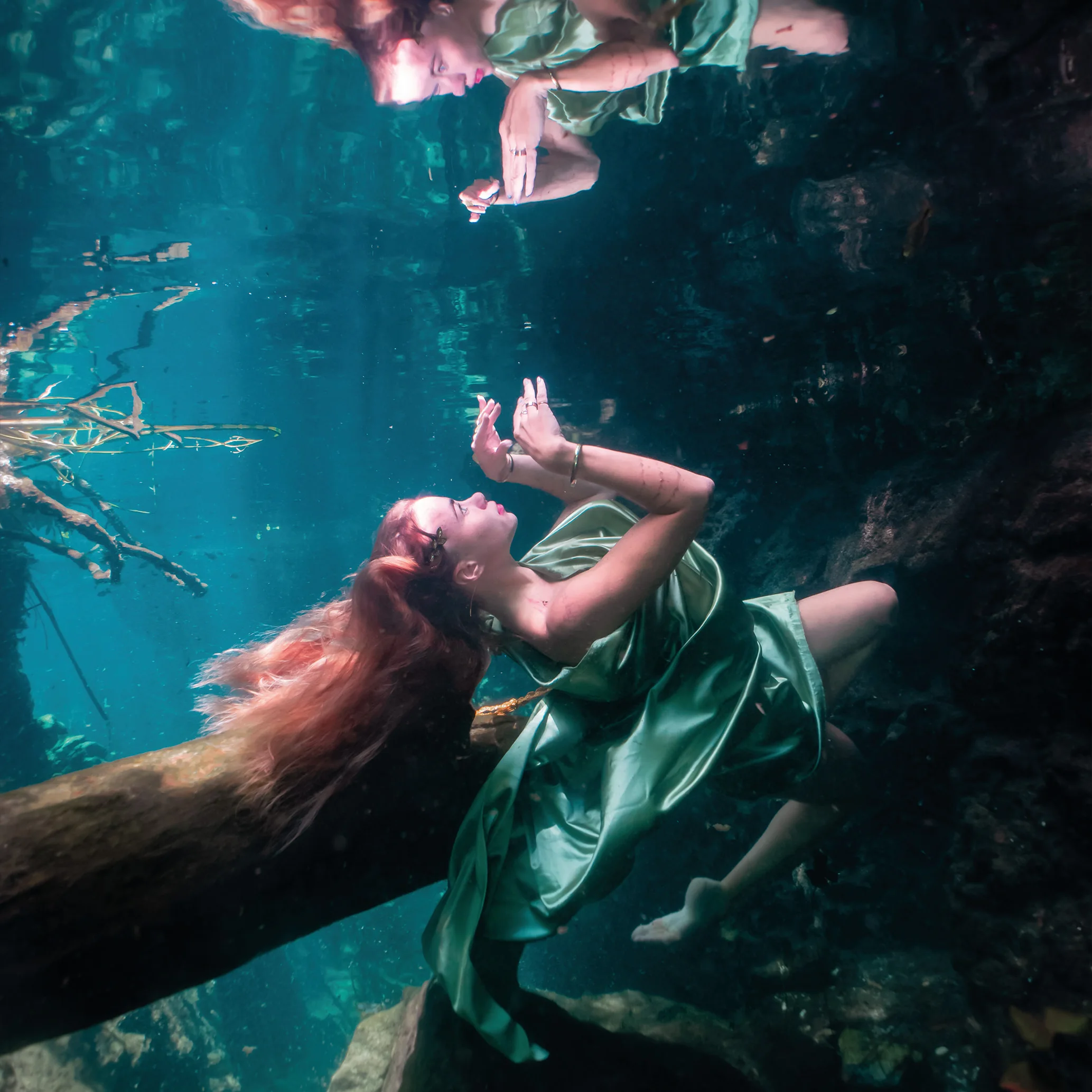 Woman in a green satin dress drifting beside a fallen branch in a cenote