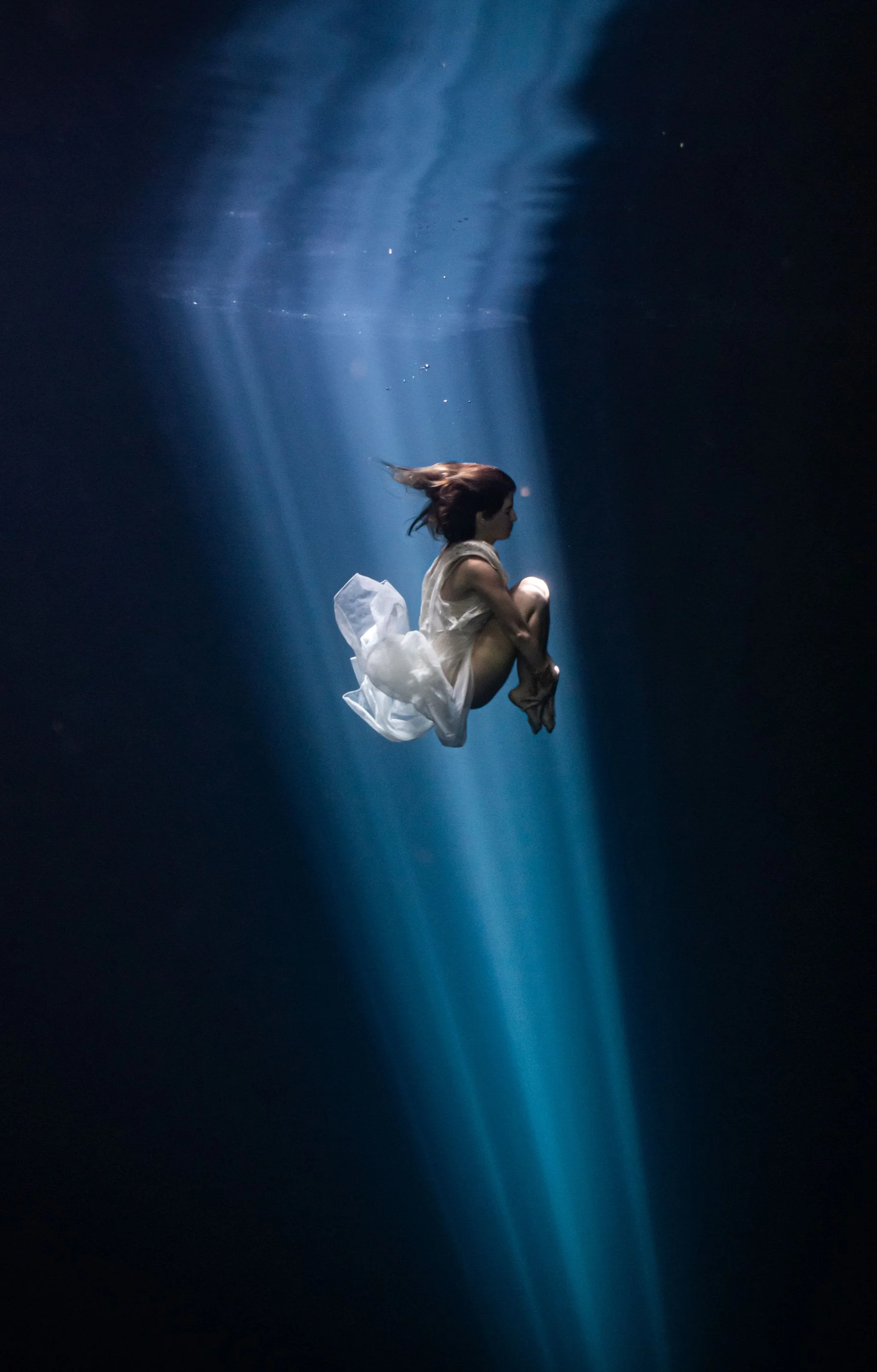 Freediver suspended in the blue light of a Tulum cenote